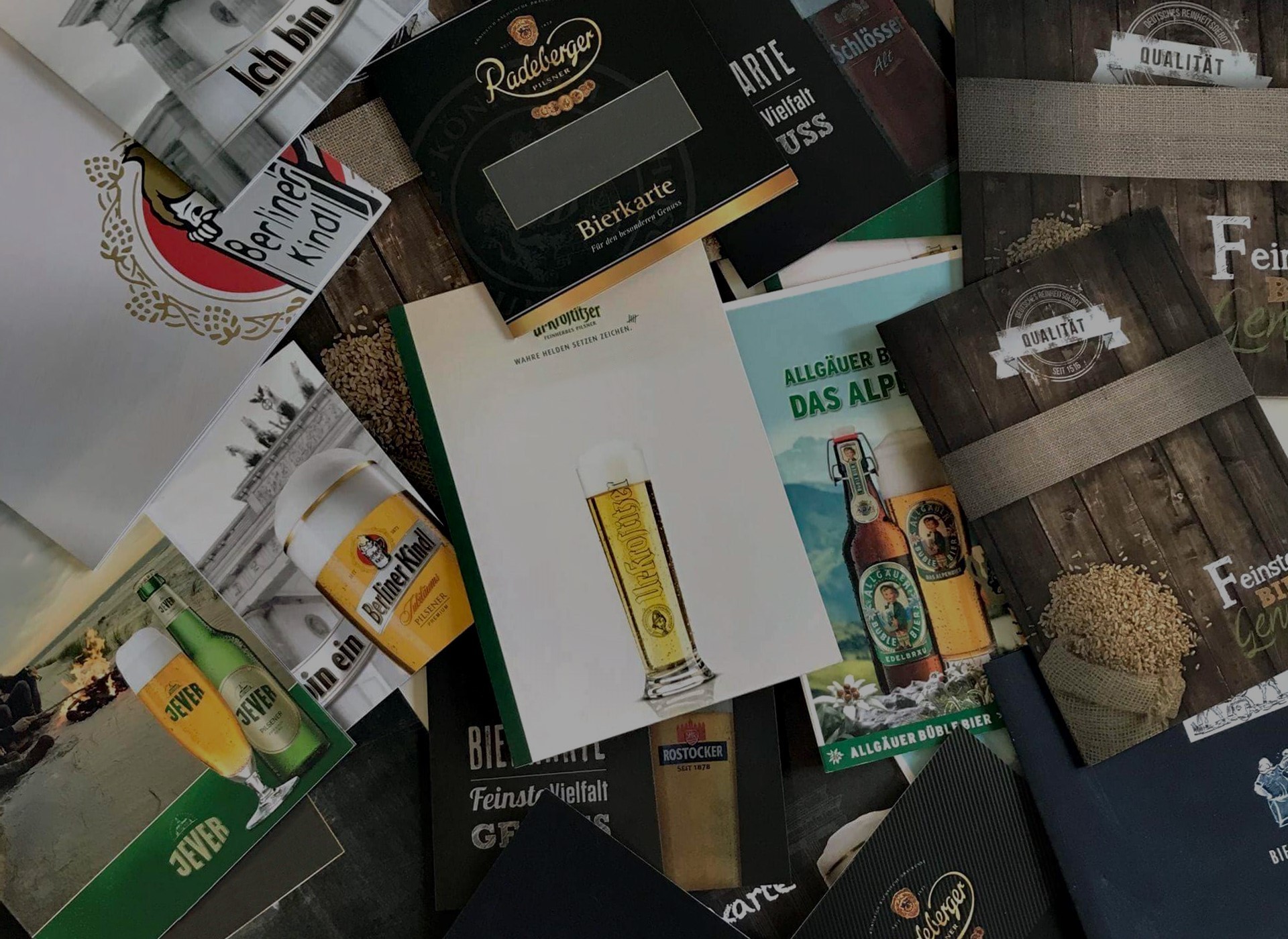 Verschiedene Werbematerialien und Biertypen liegen auf einem Tisch verteilt.